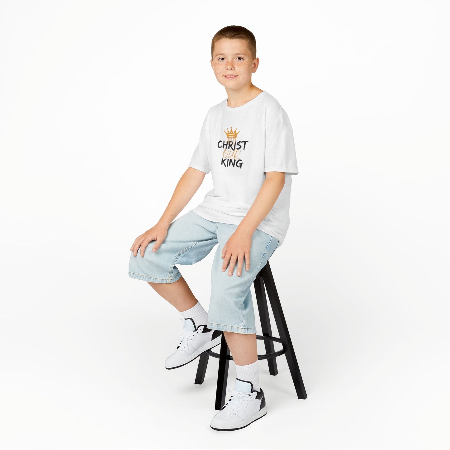 Boy wearing a white Christian junior kids t-shirt with Christ King design sitting on a black stool
