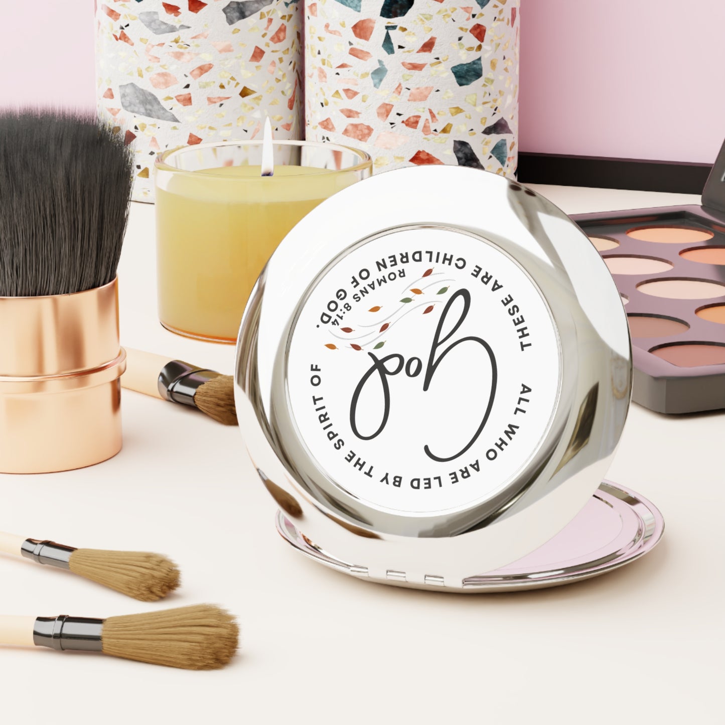 Logos Christian travel mirror with faith-inspired design placed on vanity with makeup brushes and palette