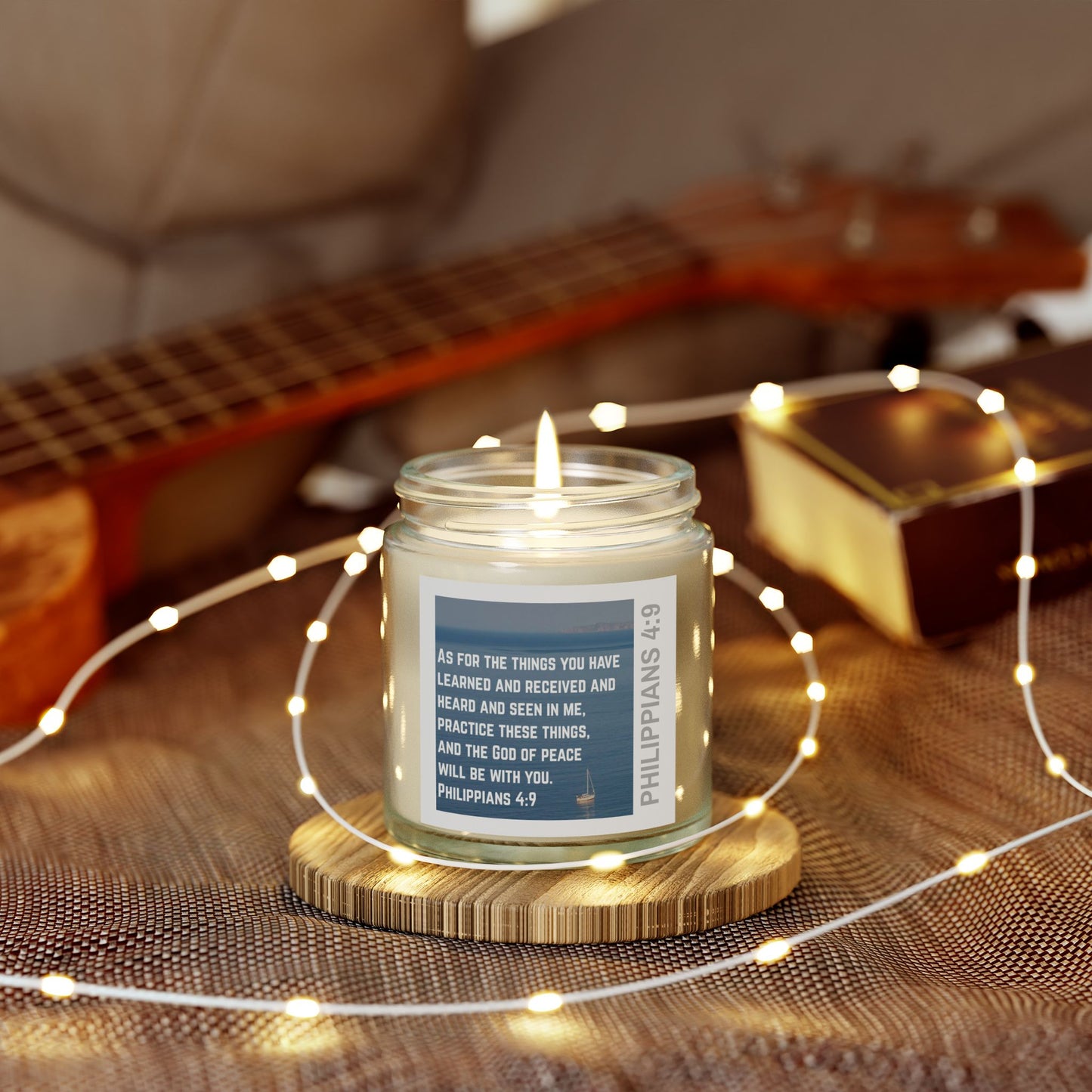 Eco-friendly Christian candle with Philippians 4:9 scripture label on wooden coaster with guitar backdrop