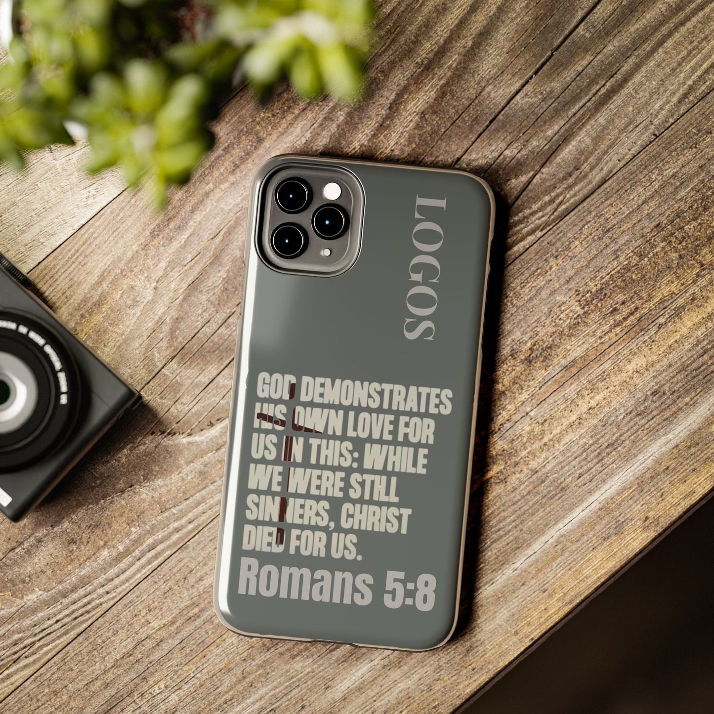Logos Christian phone case with Romans 5:8 Bible verse design on a gray background