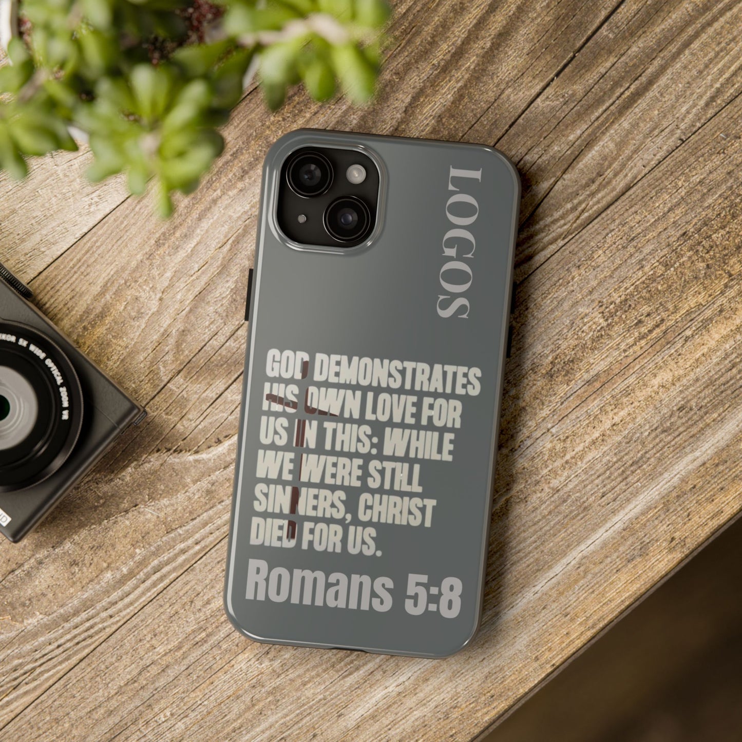 Christian phone case by Logos with Romans 5:8 scripture text on a gray background