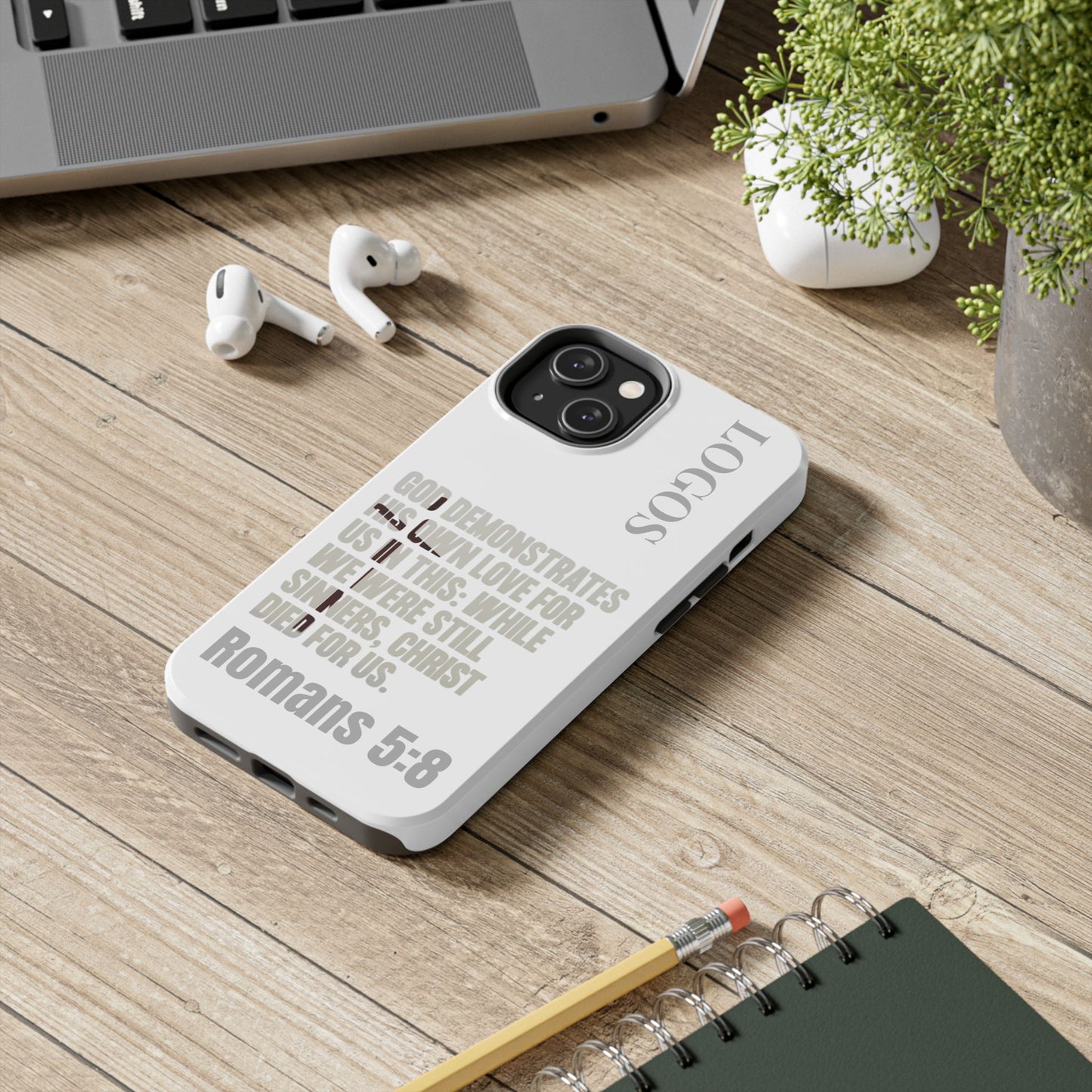 Logos Co. faith-based tough cases with Romans 5:8 Bible verse design on white phone case on wooden desk