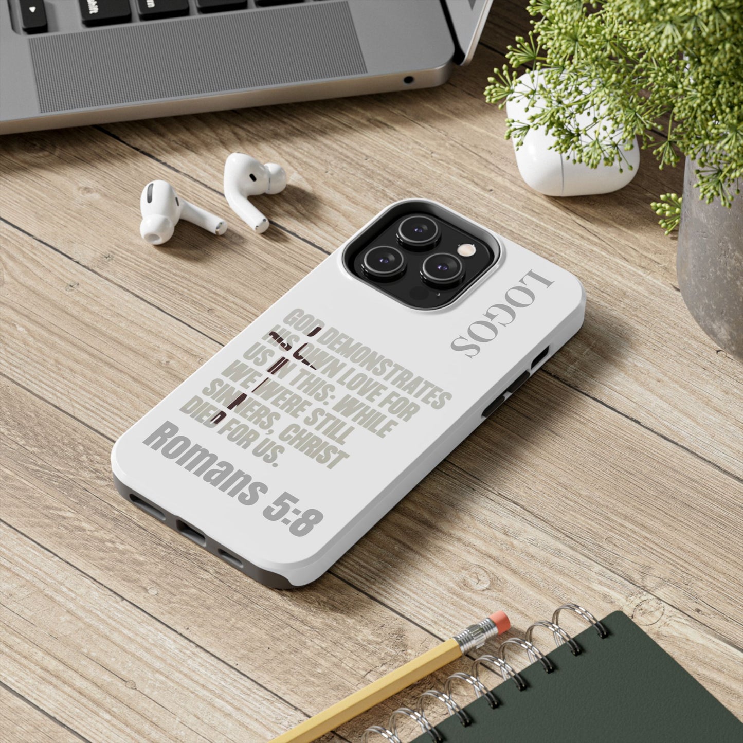 Logos Co. faith-based tough cases white phone case with Bible verse Romans 5:8 on wooden desk