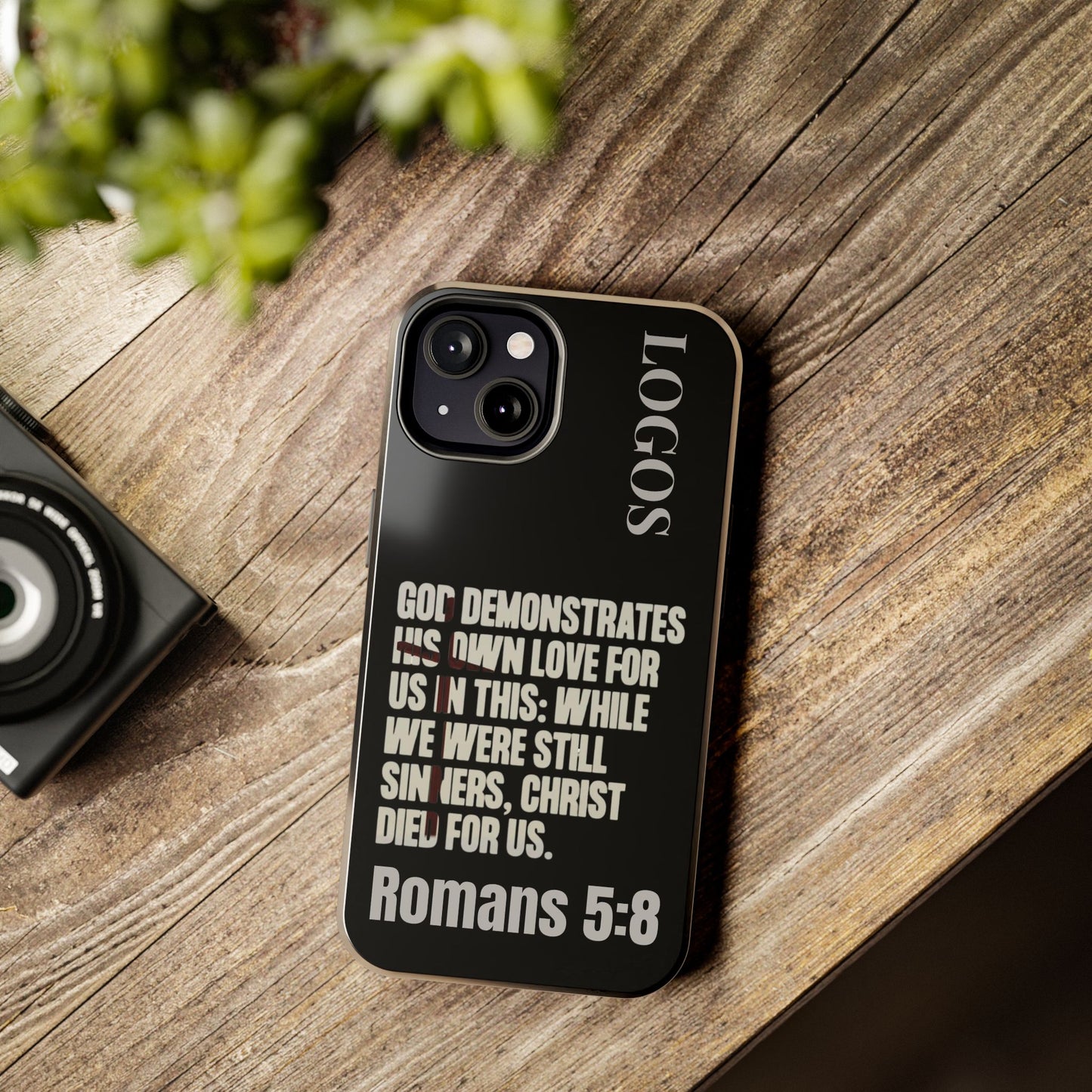 Black Romans 5:8 phone case by Logos with inspirational Bible verse design on a wooden surface
