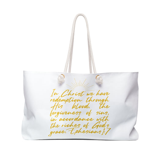 Scripture inspired travel bag with a gold text design featuring Ephesians 1:7 on a white background