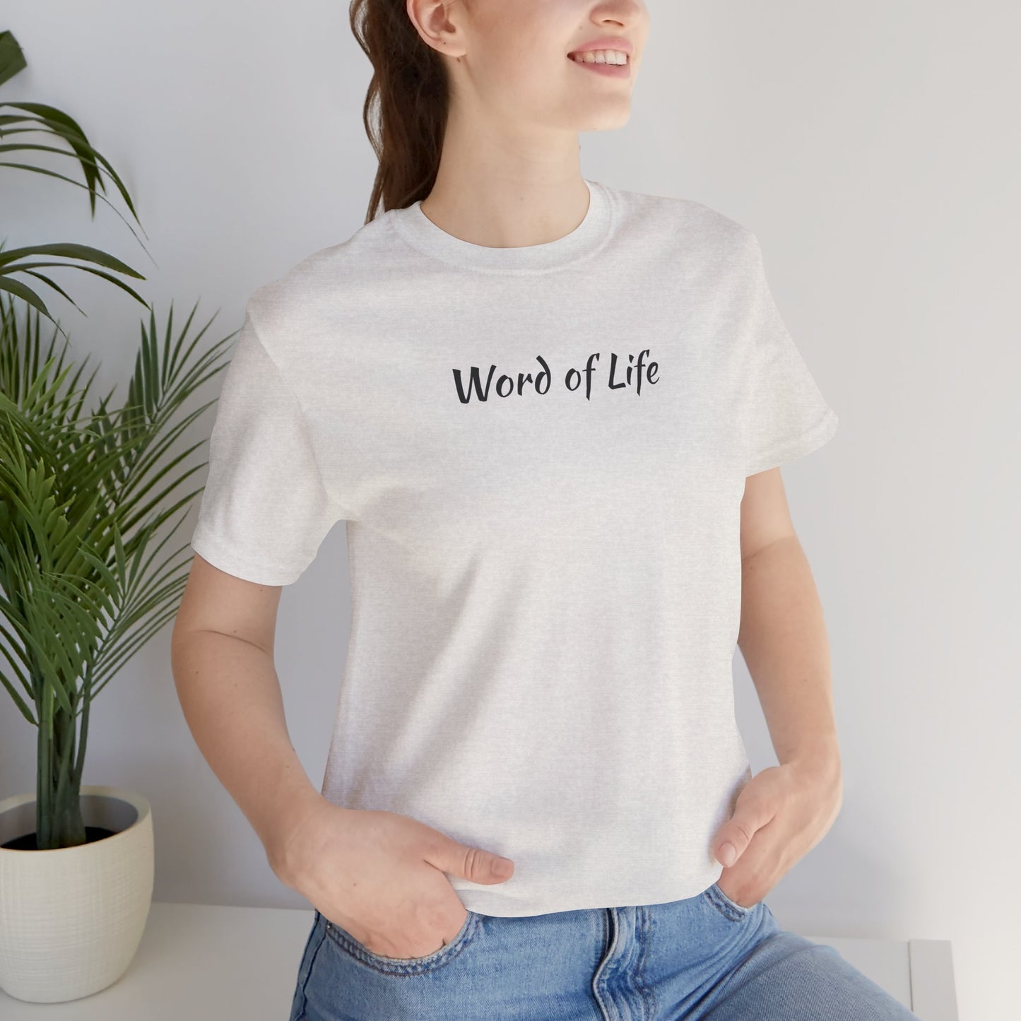 White Word of Life Christian shirt worn by woman with casual blue jeans and plant background
