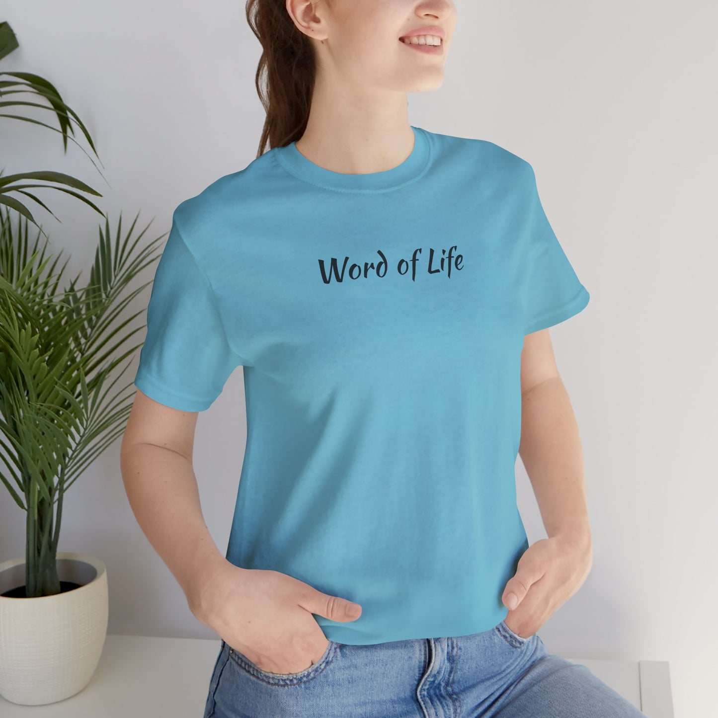Woman wearing a light blue Word of Life Christian shirt sitting beside a potted plant