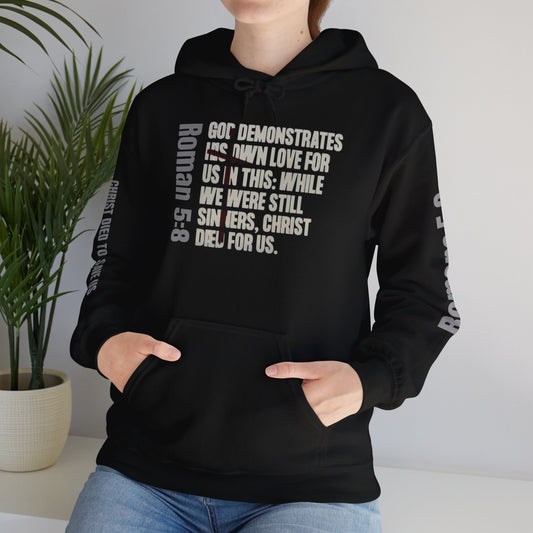Black Christian scripture hoodie from Logos Co. with Bible verse Roman 5:8 printed on front and sleeves