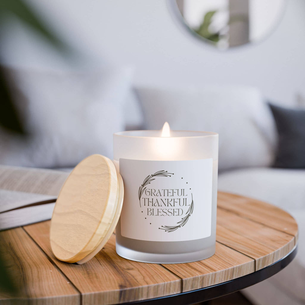 Scented candle with 'Grateful, Thankful, Blessed' phrase, frosted glass holder, and wooden lid on a table