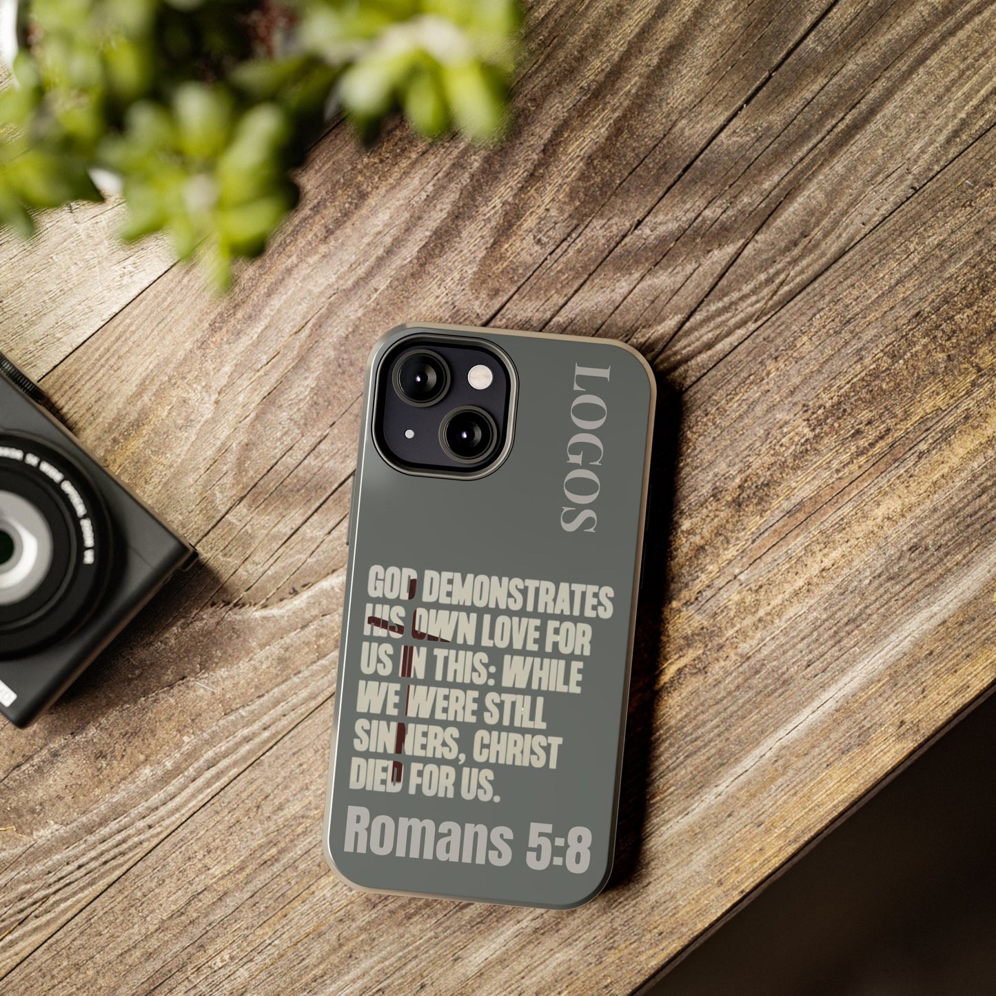 Logos Christian phone case with Romans 5:8 scripture design on a wooden table