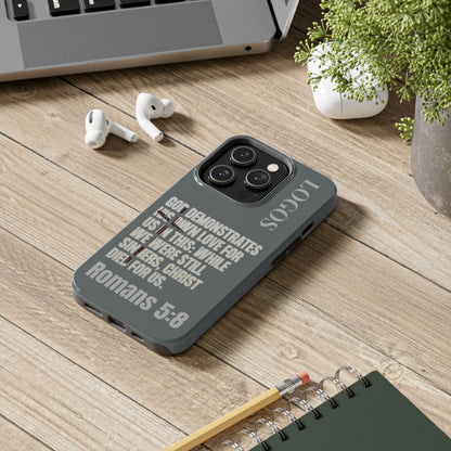 Logos Christian phone case with Bible verse Romans 5:8 in gray on a wooden desk