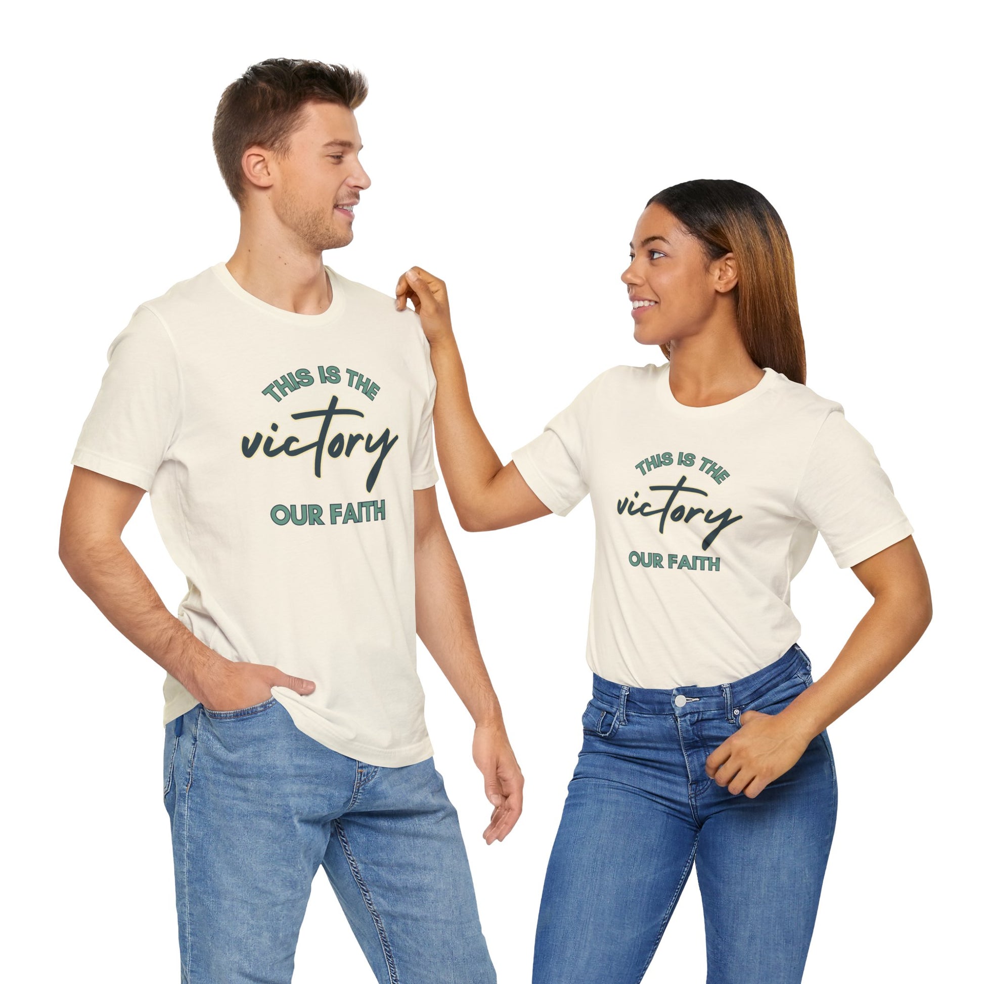 Man and woman wearing This Is The Victory T-shirt in white with faith-themed text design