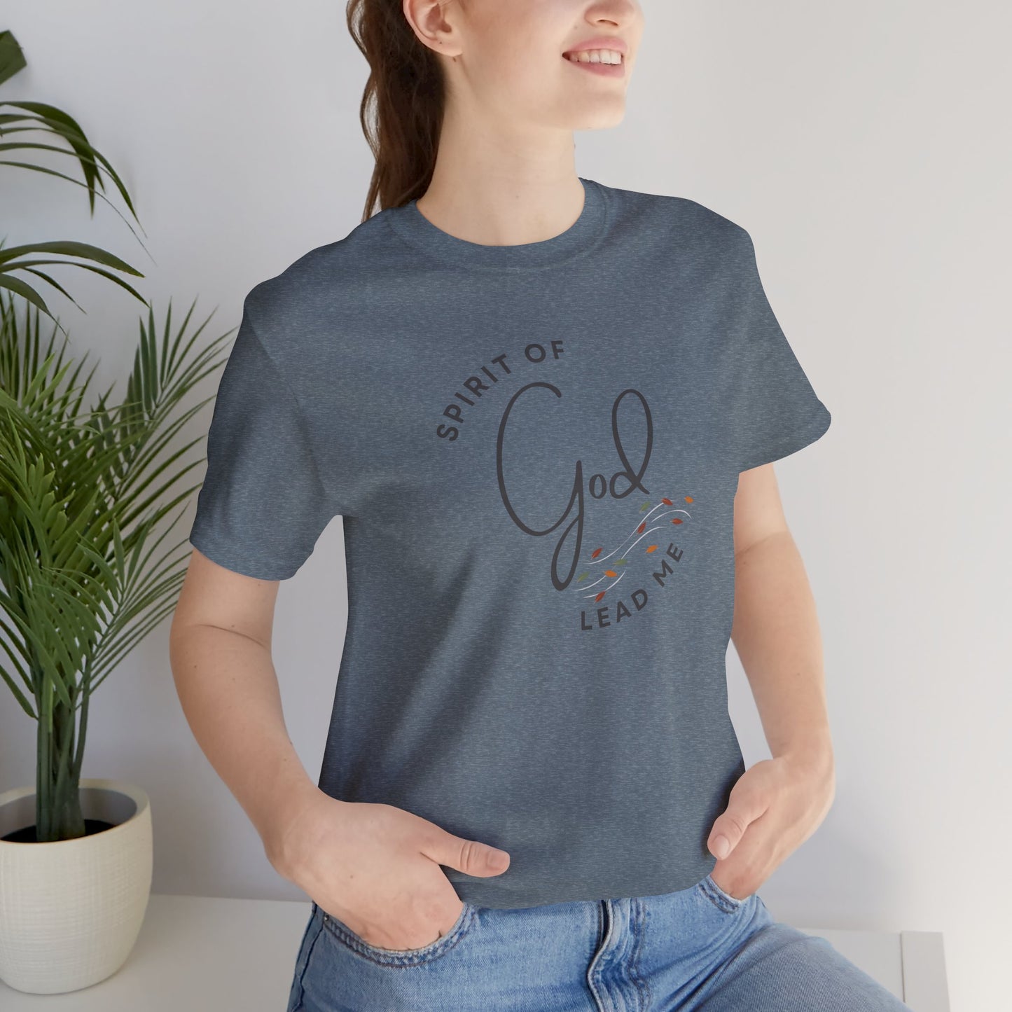 Logos Spirit Lead Me shirt in blue worn by woman with hands in pockets and plant background