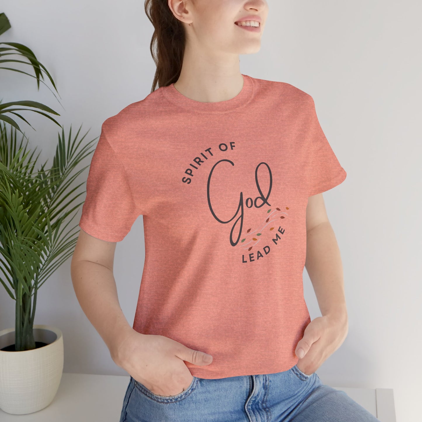 Logos Spirit Lead Me shirt in coral with faith-based text design worn by woman with hands in pockets
