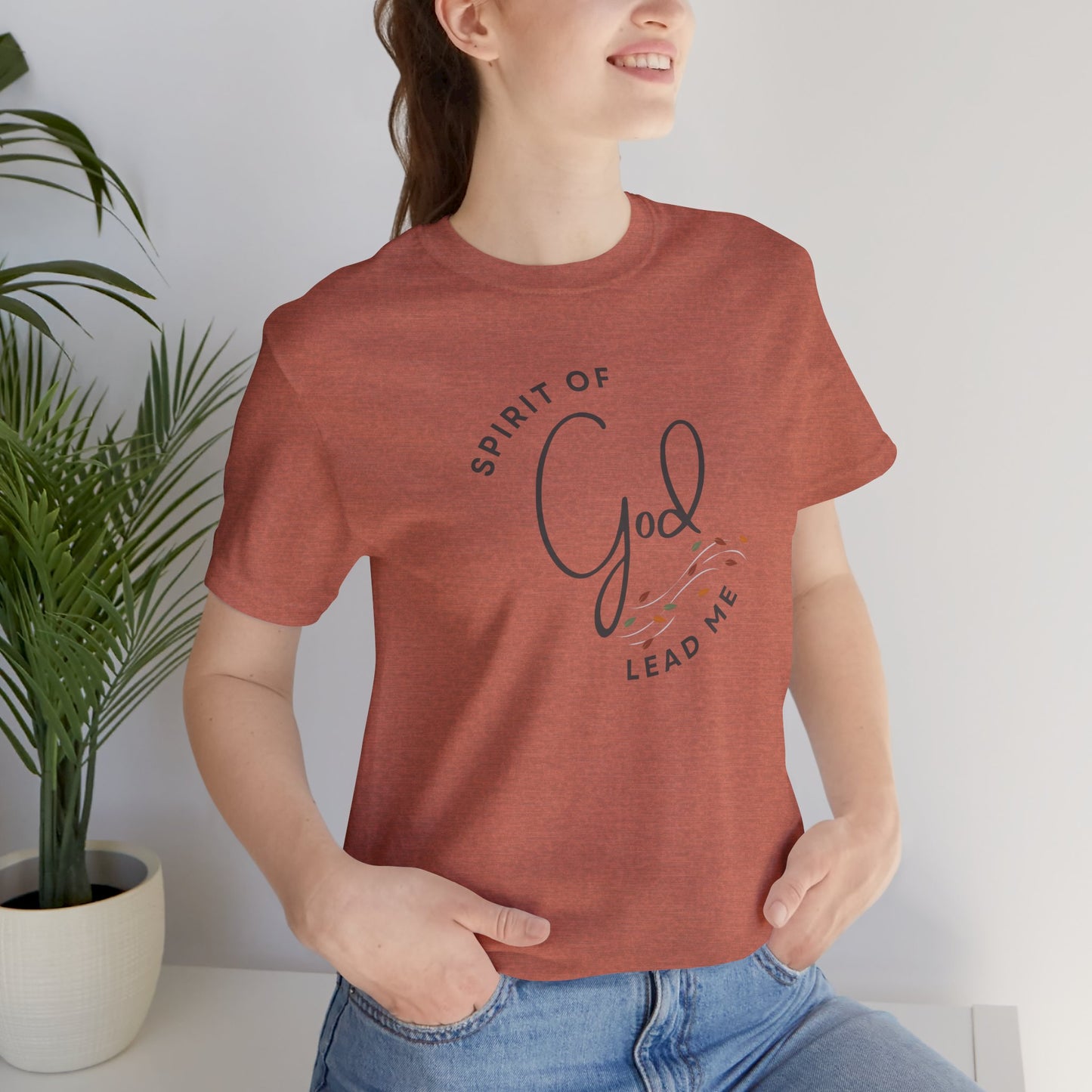 Woman wearing a rust colored Spirit Lead Me shirt with Romans 8:14 themed graphic and casual blue jeans