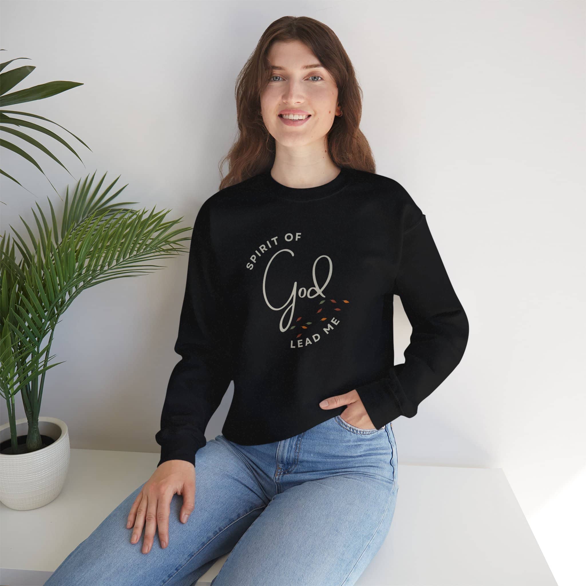 Woman wearing black Spirit Lead Me sweatshirt with God text design sitting near plant