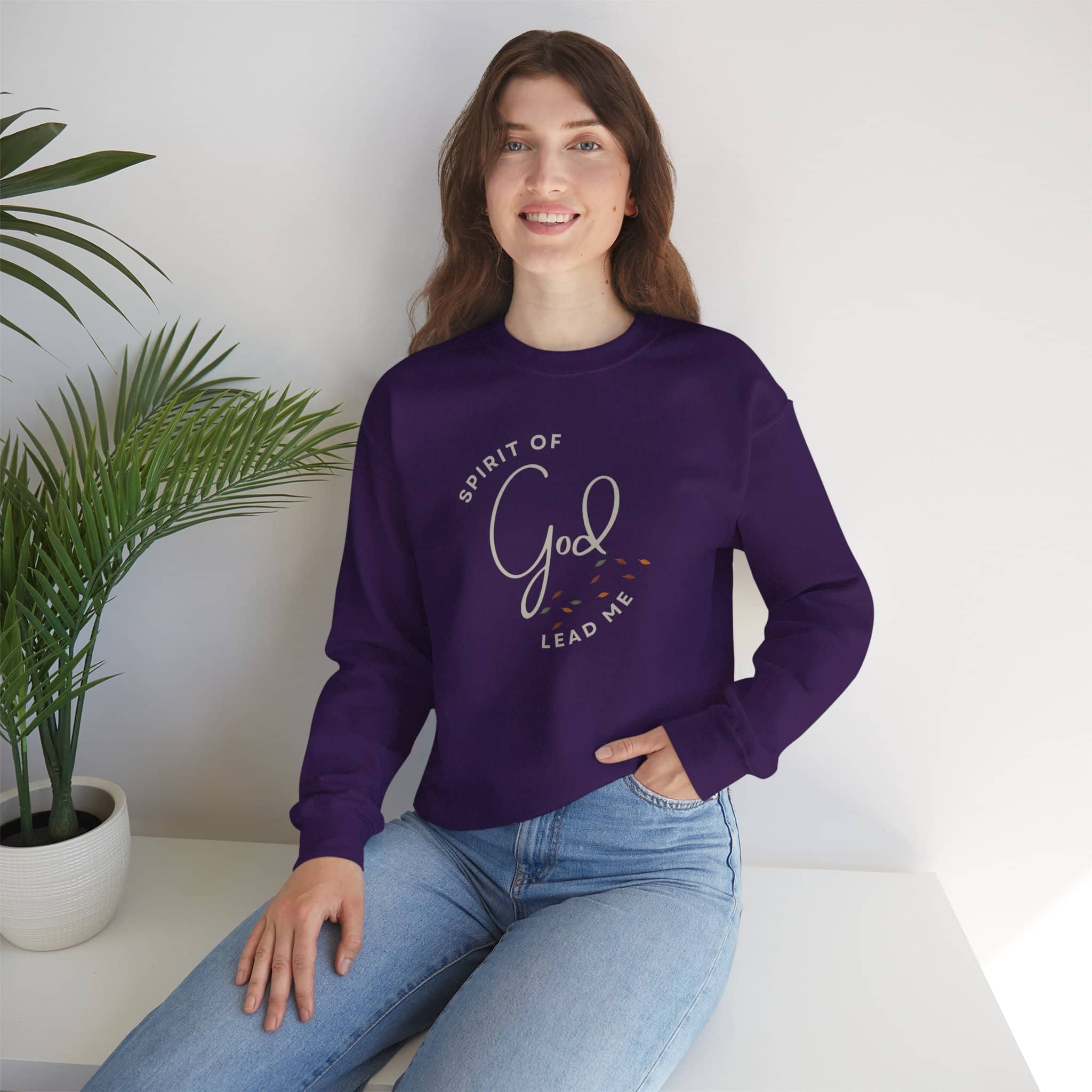 Spirit Lead Me sweatshirt in purple worn by a woman sitting next to a potted plant