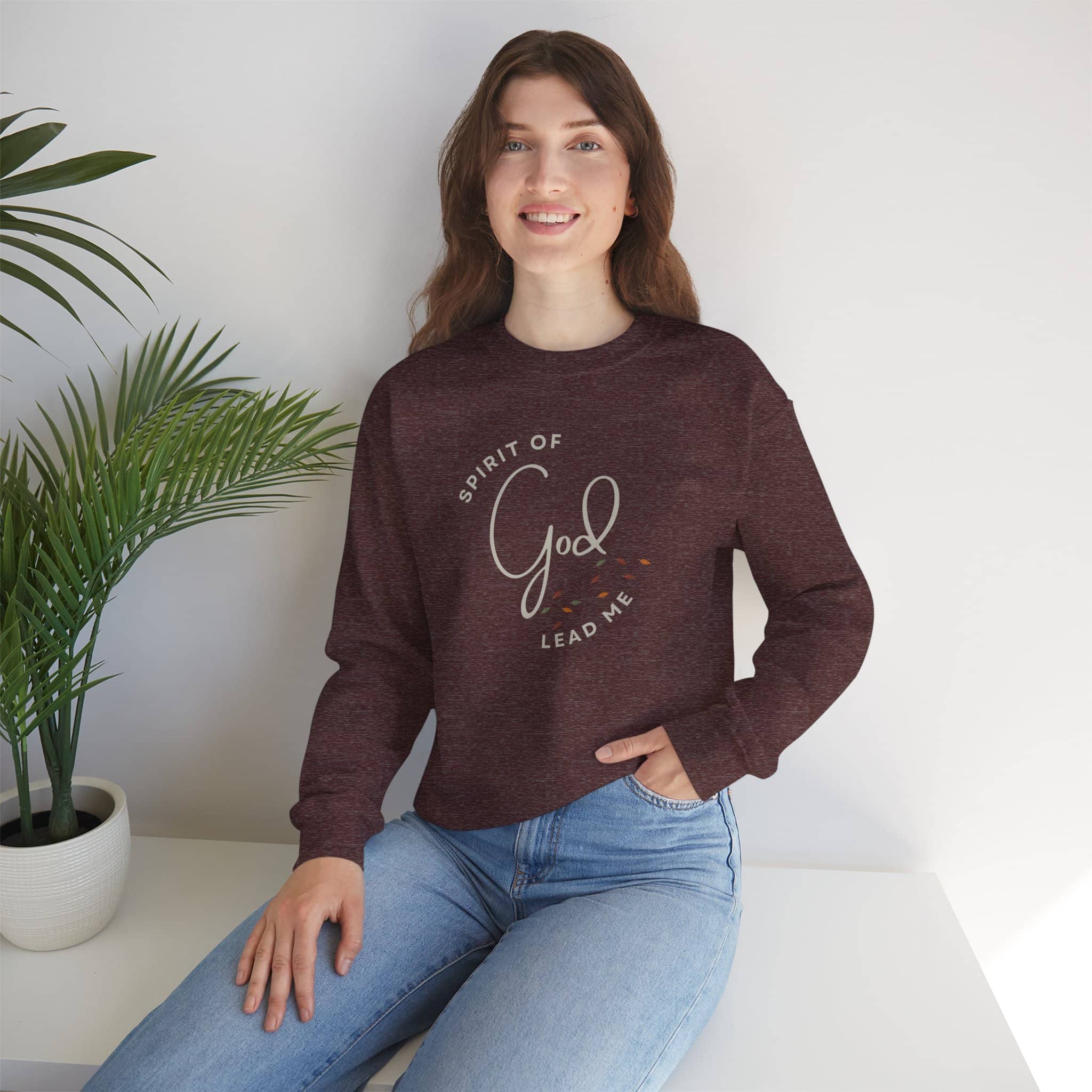 Woman wearing a maroon Spirit Lead Me sweatshirt by Logos with God script design sitting indoors