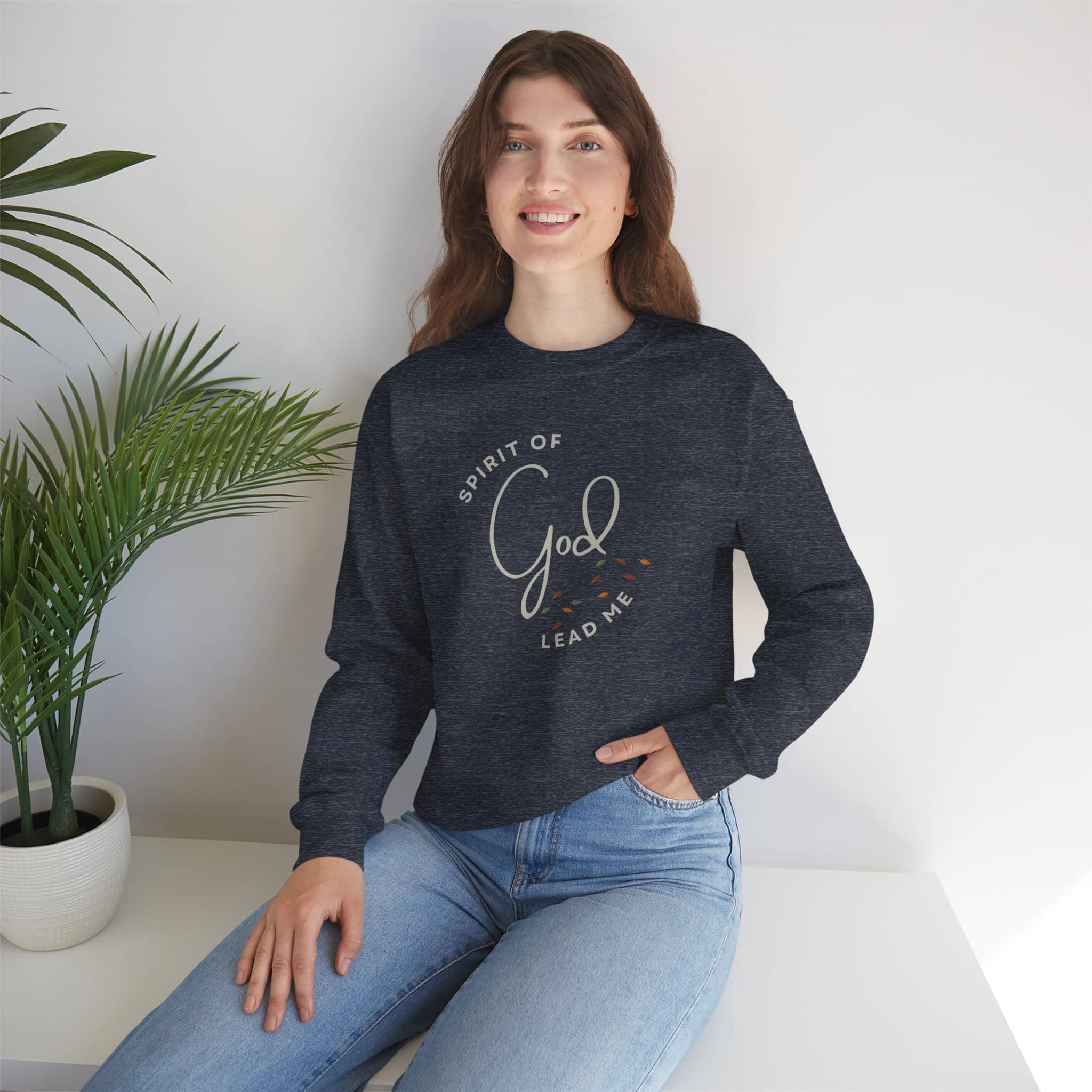 Woman wearing a navy Spirit Lead Me sweatshirt with design sitting near a plant