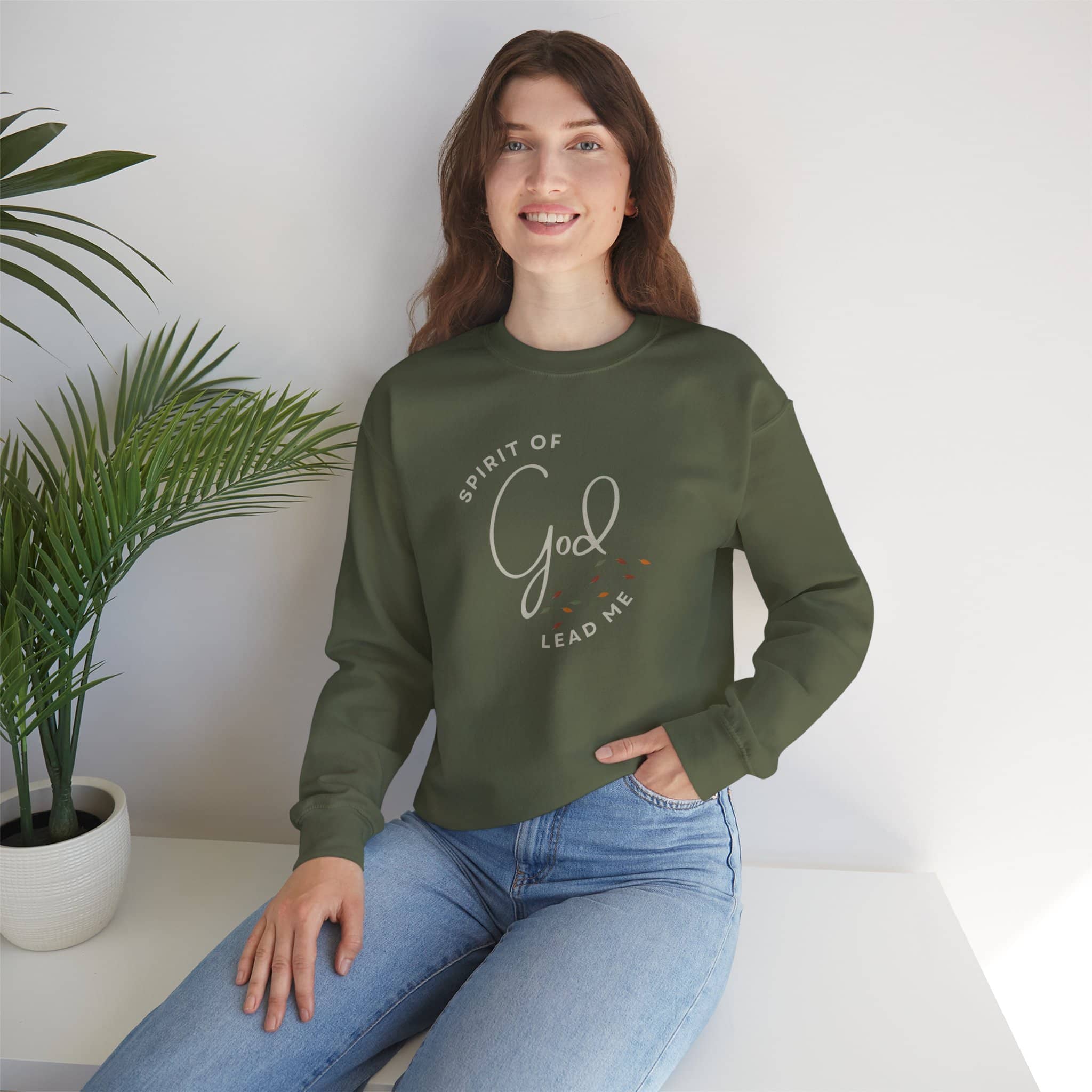 Woman wearing olive green Spirit Lead Me sweatshirt with God script design sitting indoors
