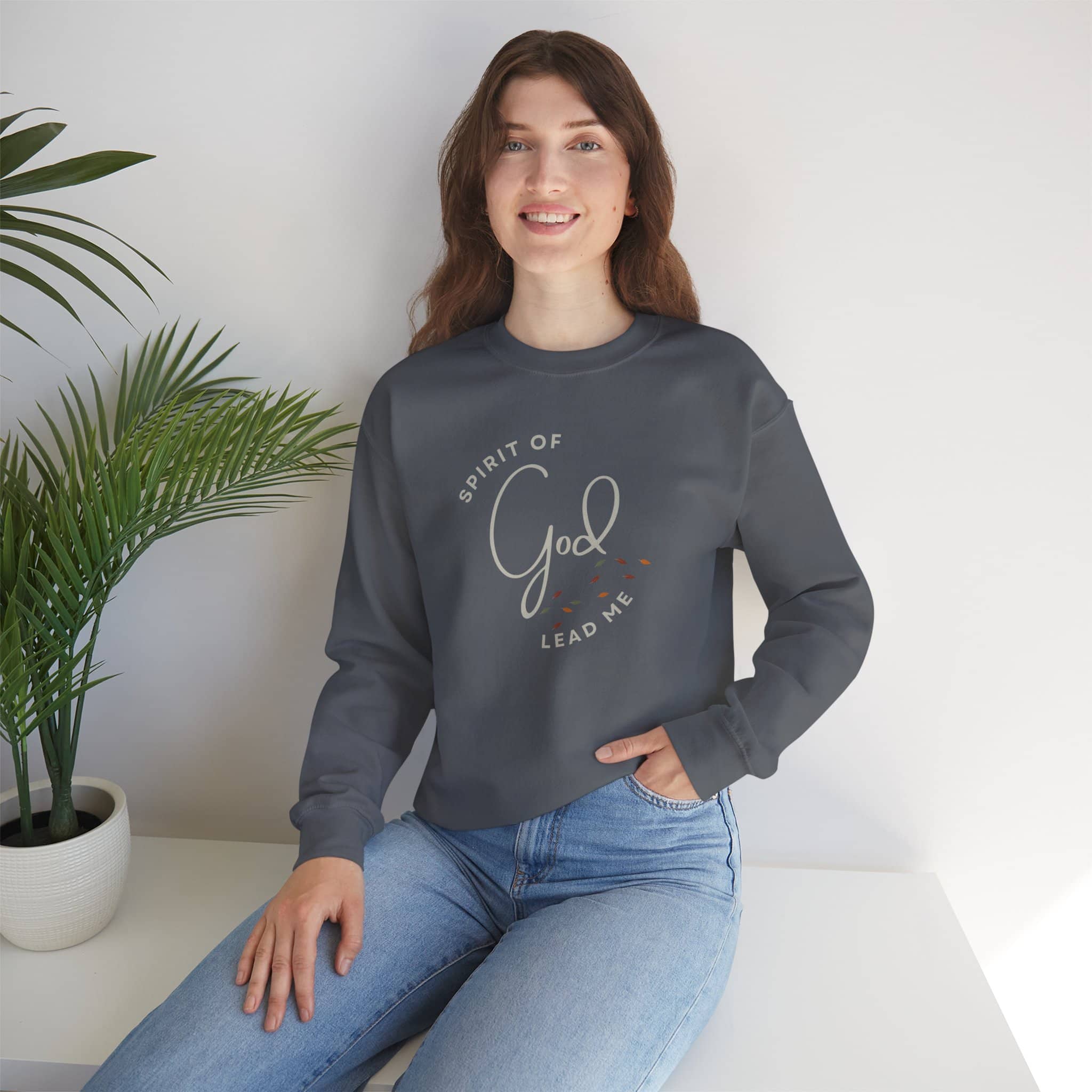 Woman wearing a dark gray Spirit Lead Me sweatshirt with script text and casual blue jeans